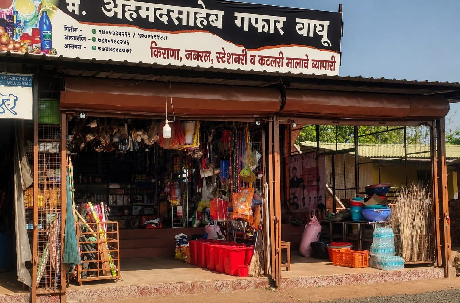 The shop's storefront in Bhambed, with the family's signboard above the entrance and daily essentials displayed outside.